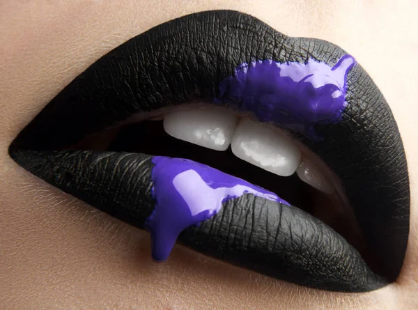 Macro and close-up creative make-up theme: beautiful female lips with black lipstick and purple liquid paint.