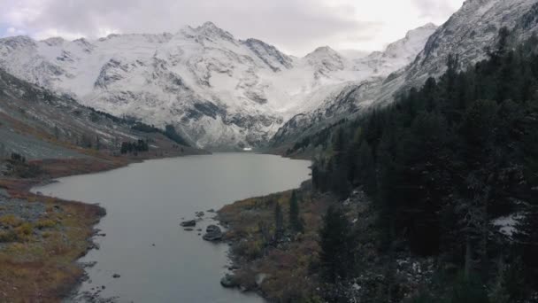 Κινηματογραφικό drone που πετά πάνω από μια λίμνη και το δάσος στα βουνά. ακτογραμμή μιας ορεινής λίμνης με βάρκες και δάση — Αρχείο Βίντεο