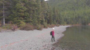 Bir dağ gölünün kıyısında sırt çantalı genç bekar bir kadın. İHA atışı.