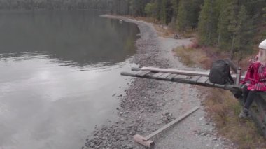 Genç kadın dağ gölünün kıyısındaki eski bir rıhtımda oturur ve içer.