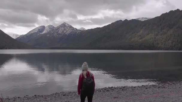 Jeune femelle célibataire avec sac à dos sur le bord d'un lac de montagne. Drone shot . — Video