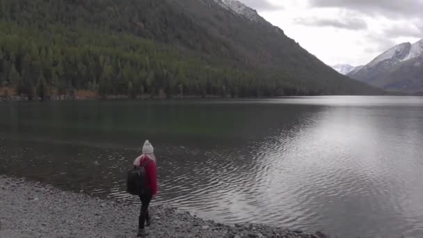 Jonge alleenstaande vrouw aan de oever van een bergmeer. Een drone schot.. — Stockvideo