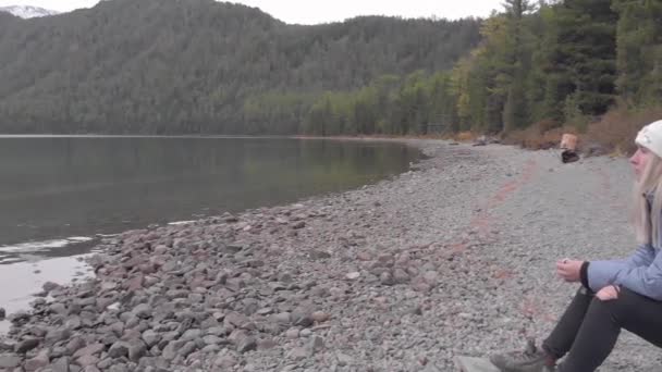 Young single female with backpack on the shore of a mountain lake. Drone shot. — Stock Video