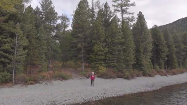 Mladá samička s batohem na břehu horského jezera. Výstřel dronů. — Stock video