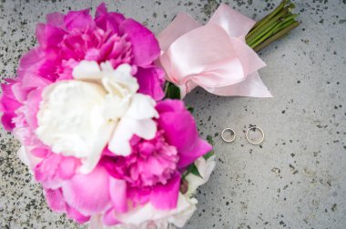 pembe bir kurdele ve hafif beton arka plan üzerinde iki altın alyans ile bağlı pembe ve beyaz şakayık düğün Gelin buketi