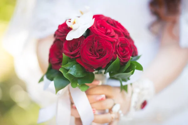 red Bridal bouquet in the hands of the bride in a white dress