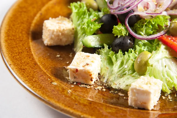 Yunan salatası yakın plan. Sağlıklı beslenen zeytin, peynir, yeşillikler, marul, soğan, domates, iştah açıcı bir şekilde kahverengi bir tabakta servis edilir.