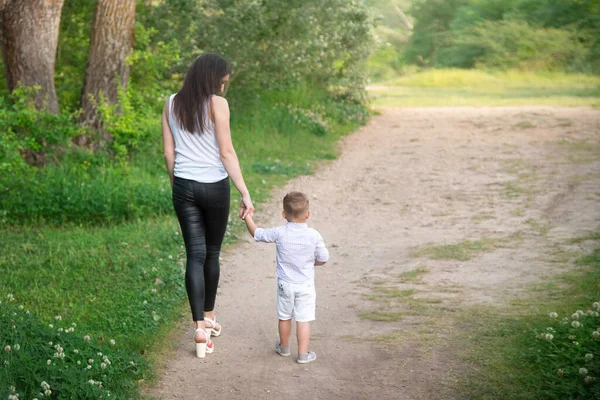 Anne ve çocuk geniş bir yolda yürüyorlar. Ebeveynlerin güvenini ve desteğini. Çocuk genç bir kadının elini tutuyor. Gezinti.