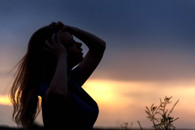 Mavi gökyüzüne karşı tarlada turuncu bir günbatımının arka planında duran bir kızın koyu gölgesi. Yarı-yanal çizgiler.