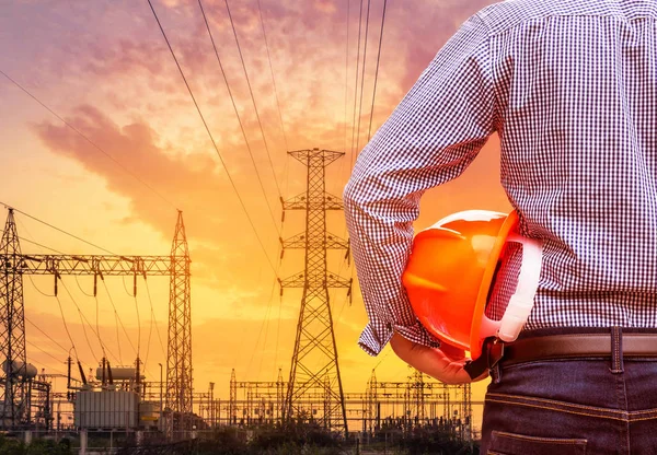 yüksek gerilim elektrik pilon ayağı ile sarı kask içinde elektrik santraller Trafo Merkezi günbatımı zamanında tutan mühendisi