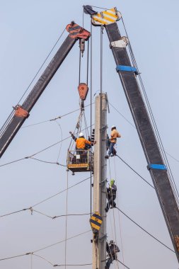Çalışma yüksekliği büyük vinçler ve sepet üzerinde mavi gökyüzü ile beton elektrik enerjisi direğe tırmanma elektrikçiler 