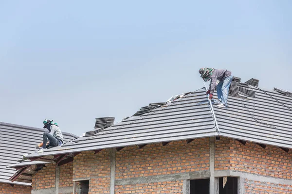 Workers installing concrete tiles on the roof while roofing house