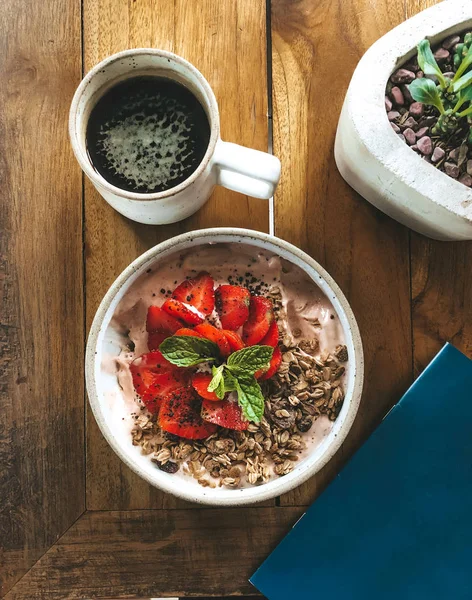 Flat Lay. Tropisk smoothie Bowl med jordgubb, banan, granola, mynta och exotiska frukter, och kopp kaffe på ett trä soffbord. Hälsosam frukost, topputsikt — Stockfoto