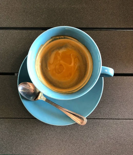 Черный кофе в синей кружке на деревянном столе с ложкой — стоковое фото