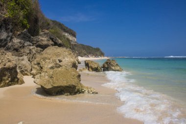 deniz ve mavi gökyüzü ile kumlu plajda kayalar güneş ışıklı