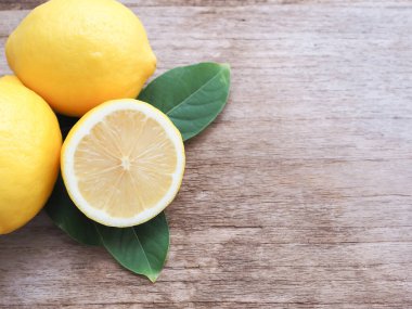 Yarım ve bir grup taze limon ve ahşap zemin üzerinde fotokopi alanı olan yapraklar. Yüksek C vitamini, ağırlığı kontrol eder ve kanser riskini azaltır. Metin için alanı kopyala