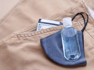 Alkol şişesi jeli, mavi kumaş yüz maskesi ve uzun pantolon arka planında para klipsi. Evden her çıkışında kirliliği ve virüsleri önlemek için kullanılmalıdır. Sağlık hizmetleri, yeni normal kavramlar
