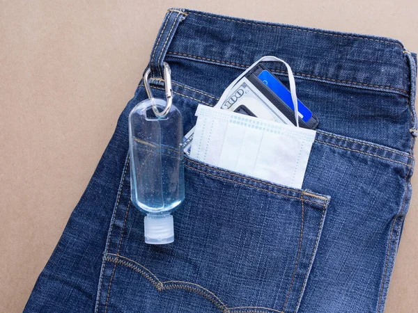 Protective face mask and Alcohol bottle gel with money clip in pocket jeans on a brown background. Every time leaving the house must be used to prevent pollution and viruses. Healthcare, New normal concepts
