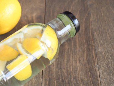 Su ve limonlar ahşap bir arka planda şişeleri dilimlerler, detoks için içerler ve vücudu tazelerler.