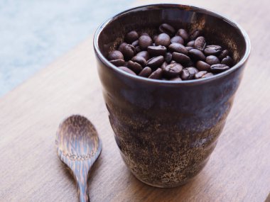 Kavrulmuş kahve çekirdekleri. Alnında eski kil bardakta. Masa arkasında tahta kaşık var.