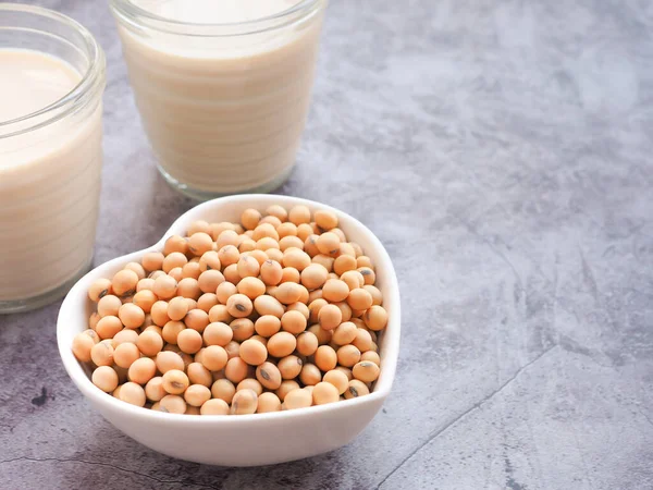Kalp şeklinde bir kasede soya fasulyesi ve gri beton arka planda soya sütü. Bitki proteini. Metin için alanı kopyala