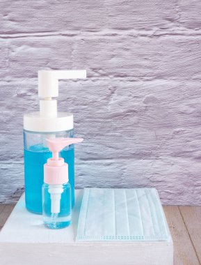 Beyaz ahşap arka planda koruyucu yüz maskesi olan pompadaki alkol jeli ve el sabunu kutusu. Sağlık kavramı.