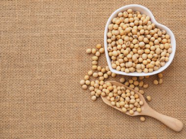 Kalp şeklinde bir kasede soya fasulyesi ve çuval bezinde ahşap kepçe. Sağlıklı gıda konsepti. Bitki proteini. Kopyalama alanı olan üst görünüm.