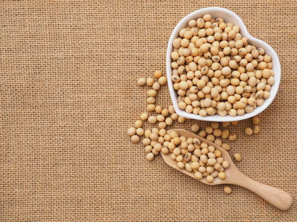 Kalp şeklinde bir kasede soya fasulyesi ve çuval bezinde ahşap kepçe. Sağlıklı gıda konsepti. Bitki proteini. Kopyalama alanı olan üst görünüm.