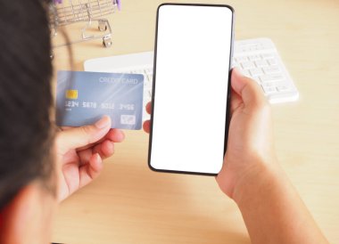 Elinde boş ekranlı akıllı telefon ve ofis masasında kredi kartı modeli olan bir kadın.