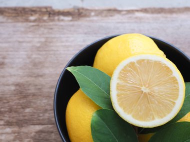 Tahta zemin üzerinde siyah kâse yaprakları olan yarım ve bir grup taze limon. Uzayı metin için kopyala. Yüksek C vitamini, yukarıdan görünüm