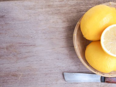 Limon meyvesi ve yarısı hasır sepetin içinde, ahşap arka planda bıçakla, mesaj için uzayı kopyala. Üst görünüm