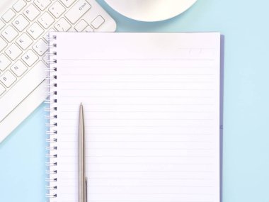 Düz mavi ofis masaüstü, boş defter ve klavyeli kalem. Metin için boşluk olan üst görünüm. İş ve eğitim kavramı