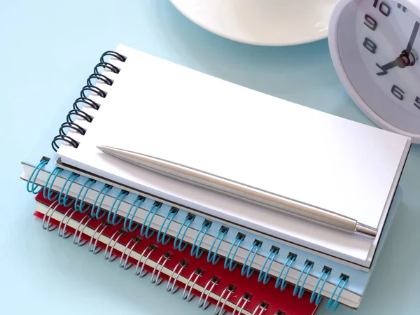 Stack blank notebook and pen with clock at 7:00 am on the blue workplace desk table. Business and education concept. Space for text