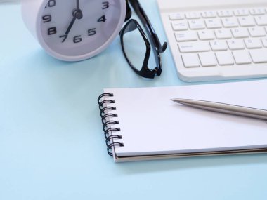 Sabah 7 'de mavi çalışma masasında defter, kalem, gözlük, klavye ve saat var. İş ve eğitim kavramı. Metin için boşluk
