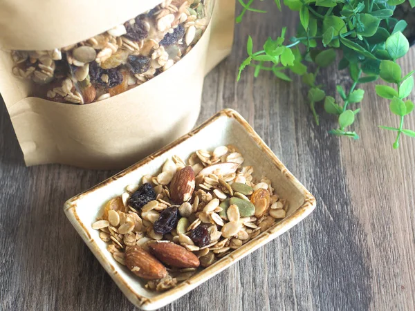 Açık kahverengi kare bir tabakta granola şeffaf bir pencere halısı kağıt perde ve ahşap masada küçük ağaçlar. Mesajın için yer aç. Sağlıklı yemek..