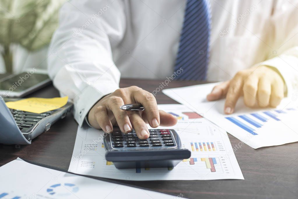 Businessman pushing and pressing on calculator and looking on business paper, finance concept on working table