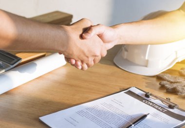 Mimarlık mühendisi, inşaat sahasında, parterde ve takım çalışması konseptinde yeni inşaat projesinde başarılı istihdam sonrasında işe alım sözleşmesini imzalayan yatırımcıyla el sıkışıyor