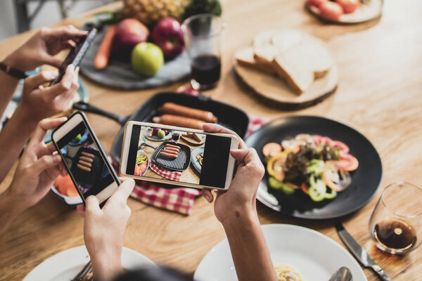 Наслаждайтесь ужином и праздником с друзьями и фотографируйтесь по телефону, чтобы опубликовать в социальной сети, вид сверху на еду на столе и группу веселых и вкусных людей
