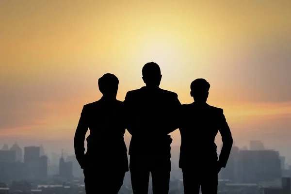 Silhouette of team businessmen stranding on top of building and looking forward, concept as set goal and teamwork concept with sun rise background