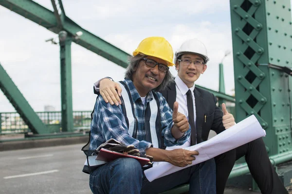 building contractor and engineer sitting and showing thumb to admire at construction working site and metal bridge