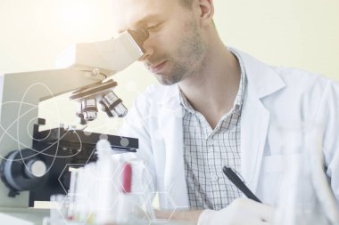 Genç adam bilim adamı veya laboratuarda araştırmacı araştırma ve mikroskop bakıyor 