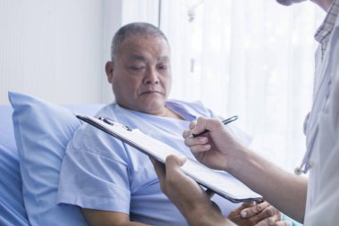 süre ayakta ve hastane yatağında eski hastaya konuşurken Pano, tıbbi formu dolduruyor doktor