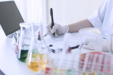 bilim adamı deney kimyasal sıvı ve laboratuvarda kağıt üzerinde bilgi yazma