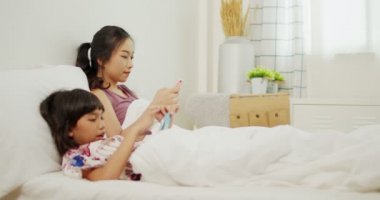 İki Asyalı kız yatakta çocuk telefonu çalar, Taylandlı kız kardeş uyumadan önce akıllı telefonlara bakar ve başkalarına sataşır.