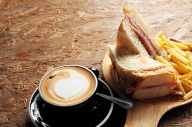 Sıcak kahve, sandviç, jambon ve peynir, kızarmış patates ahşap bir masa üzerinde.