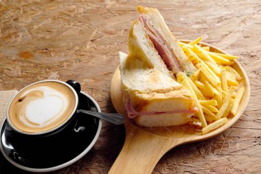 Sıcak kahve, sandviç, jambon ve peynir, kızarmış patates ahşap bir masa üzerinde.