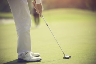 Golf oyuncusu yeşil topu deliğe sokuyor.