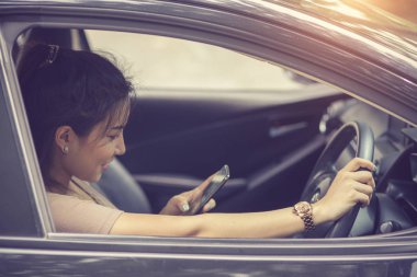 Genç kadın ile camdan gelen güneş ışığı güneşli bir günde bir araba sürüş sırasında onun smartphone vasıl arıyor