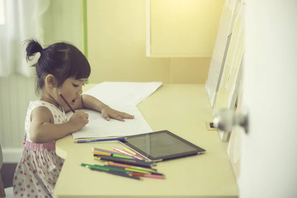 Pequena criança asiática usando um lápis para escrever no caderno no de — Fotografia de Stock