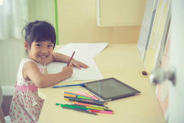 Pequena criança asiática usando um lápis para escrever no caderno no de — Fotografia de Stock